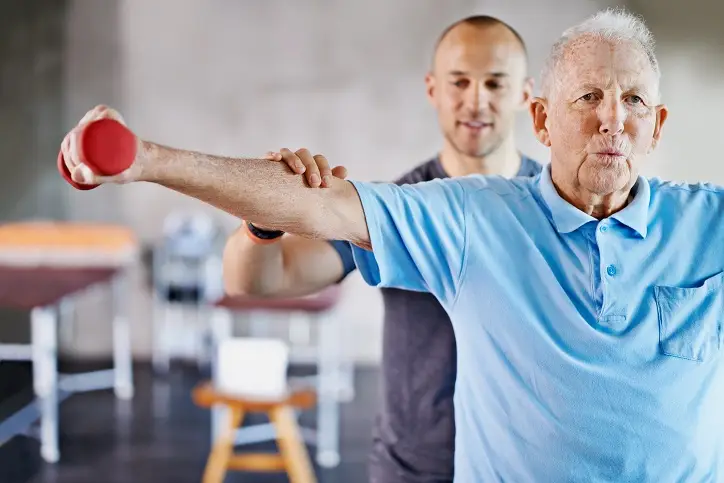 Sport-Physiotherapeut zeigt Übung älterem Mann